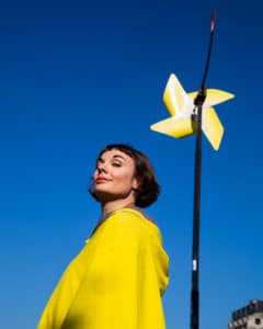Adélys in einer gelben Jacke mit einer gelben kleinen Windmühle vor einem blauen Himmel