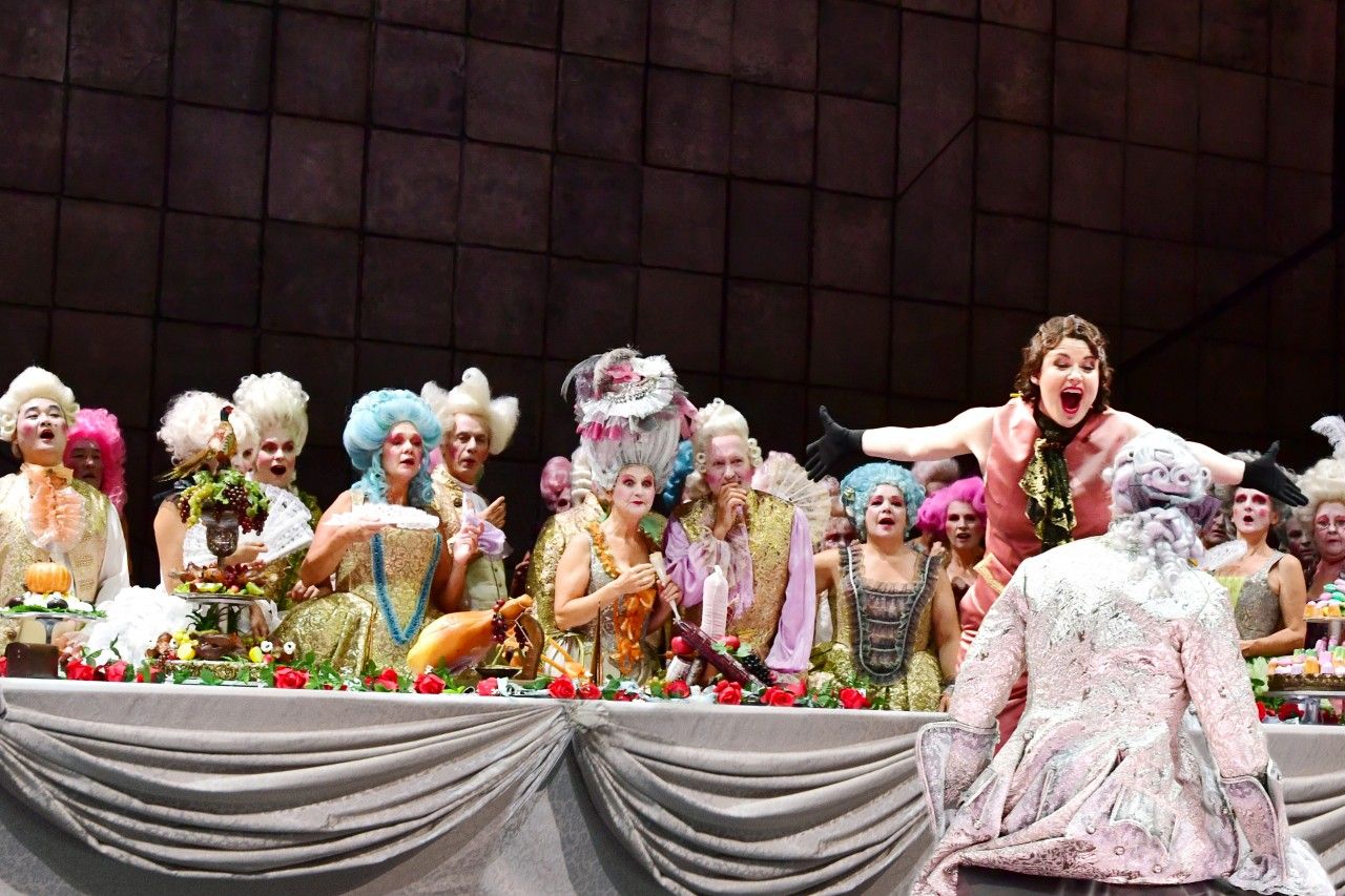 Bildbeschreibung: Eine Szene der Oper "La Juive" zeigt Männer und Frauen in bunten Kleidern an einem Bankett.